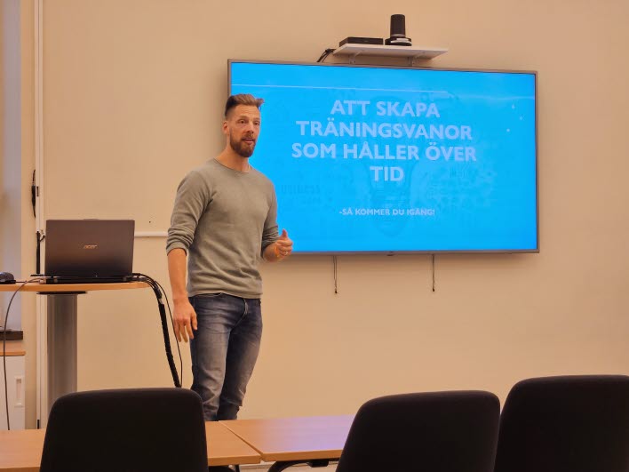 Föreläsare framför skärm med texten "Att skapa träningsvanor som håller över tid".
