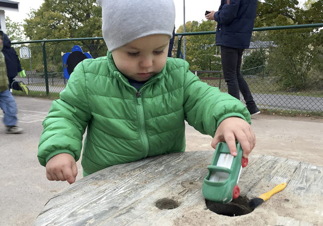 Ett barn leker med en bil utomhus på förskolan.