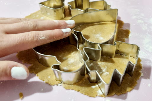 En hand trycker in pepparkaksformar i pepparkaksdegen.