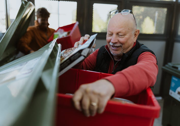 En äldre man slänger sina sopor i en stor container.