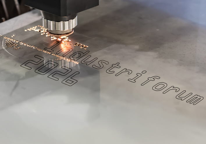 En laser skriver texten Industriforum 2026 på en mettalbit.