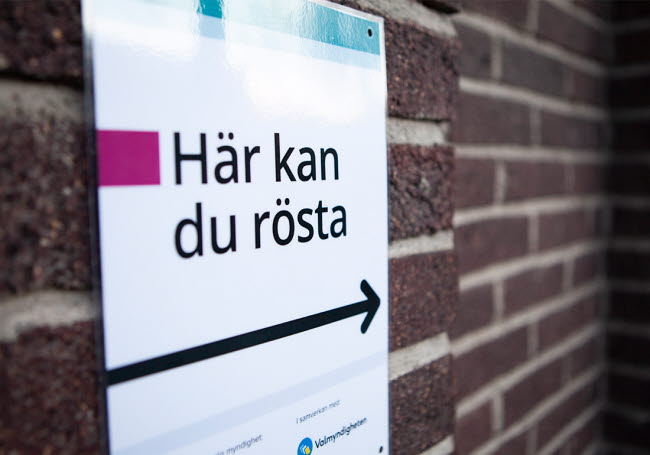 Skylt "Här kan du rösta" monterad på en vägg.