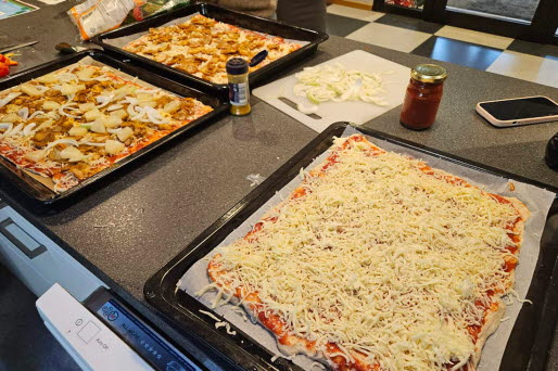 Flera plåtar med pizza, redo att bakas.