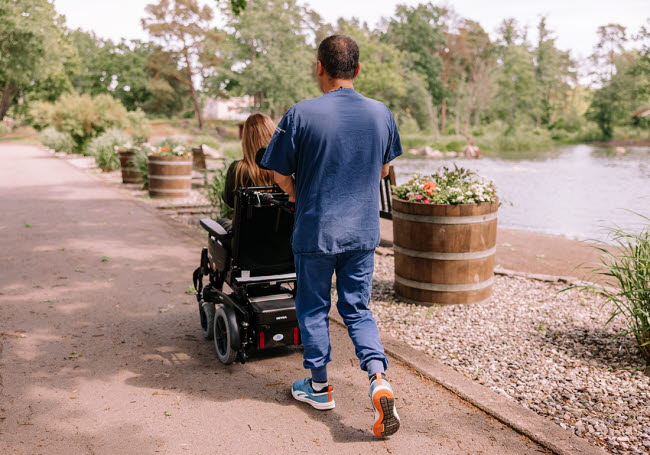 Hemtjänstpersonal på promenad med en brukare som sitter i rullstol.