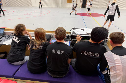 Fotbollsturnering inomhus. I förgrunden sitter några domare i bakgrunder ser man två lag spela fotboll.