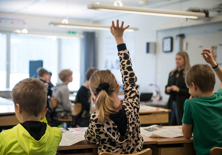 Flicka räcker upp handen i klassrum