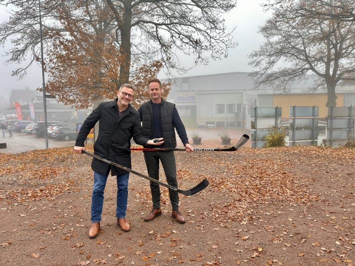 Två personer med hockeyklubbor i händerna på en grusad yta.