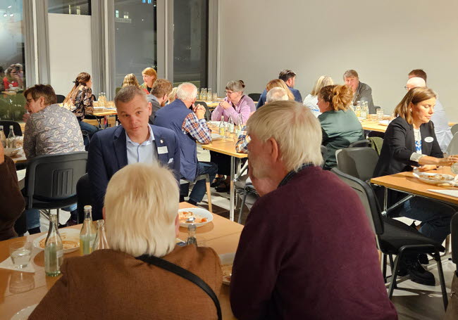 Personer sitter runt olika bord och diskuterar.