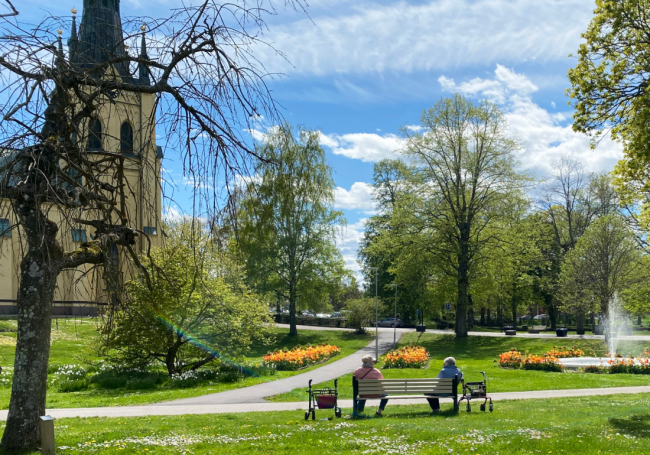 Två tanter i stadsparken sitter på en bänk och konverserar.