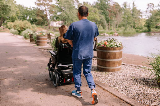 Hemtjänstpersonal på promenad med en brukare som sitter i rullstol.