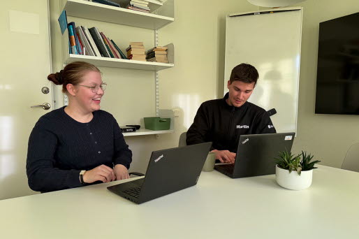 En tjej och en kille sitter vid ett bord med datorer framför sig.